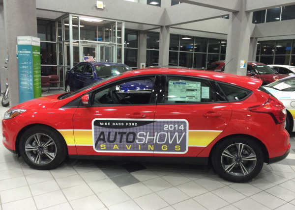 Auto event promotion sign posted on the side of a red car that was made by Oliver Signs & Advertising.