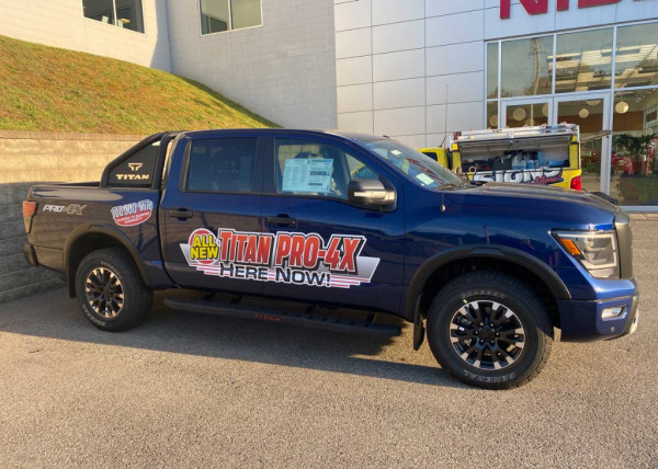 Blue truck with graphic made by Oliver Signs on the side advertising the new truck model for sale at a dealership.