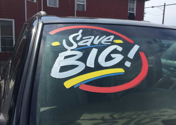 Hand-painted windshield sign says "Save Big!"