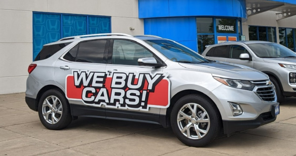 "We Buy Cars!" magnetic vehicle sign at auto dealership